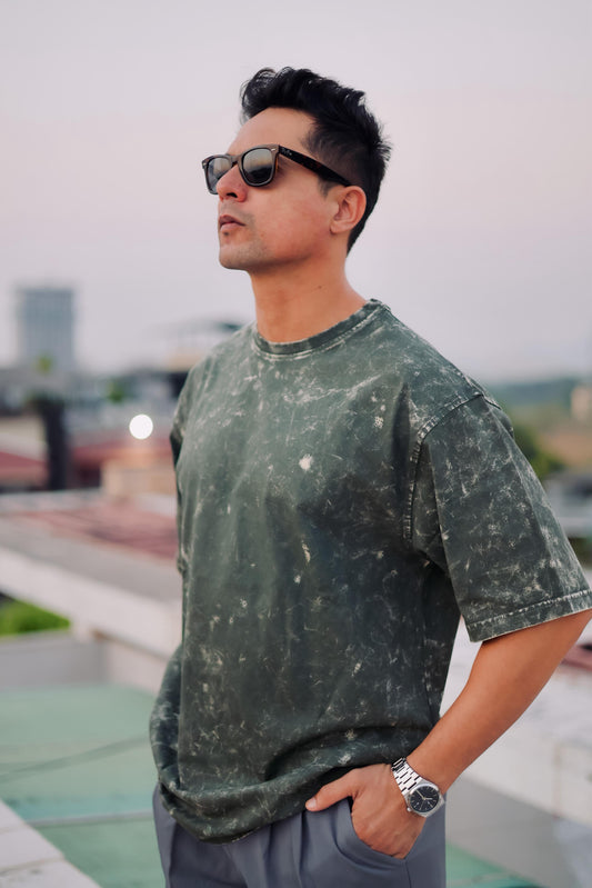 Man wearing an olive green acid wash  t-shirt and sunglasses with a blurred background